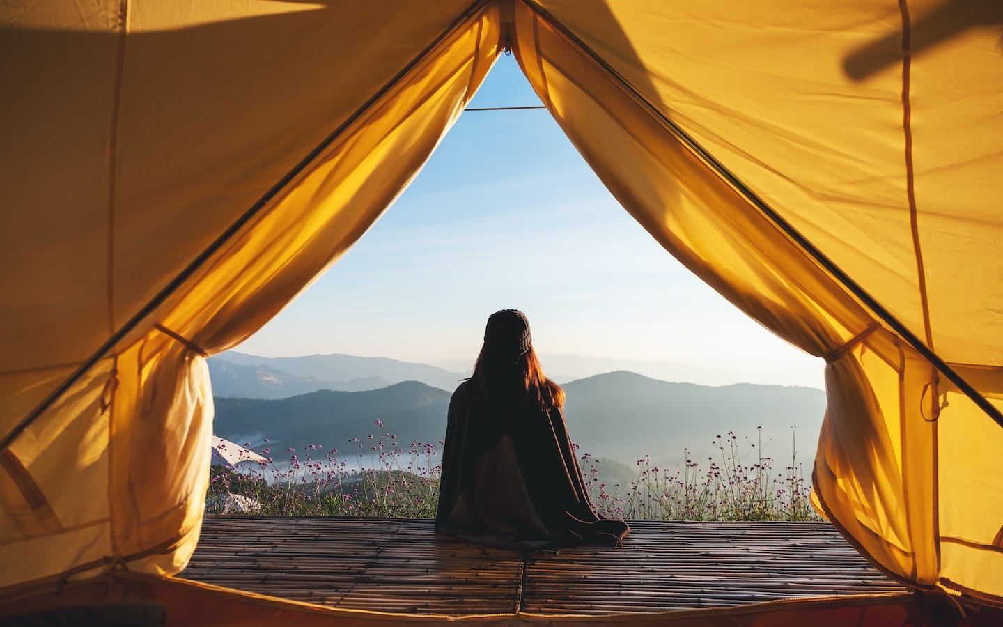 A person sitting at the entrance of a tent overlooking a mountain vista, suggesting considering the location when learning how to choose the right resort.