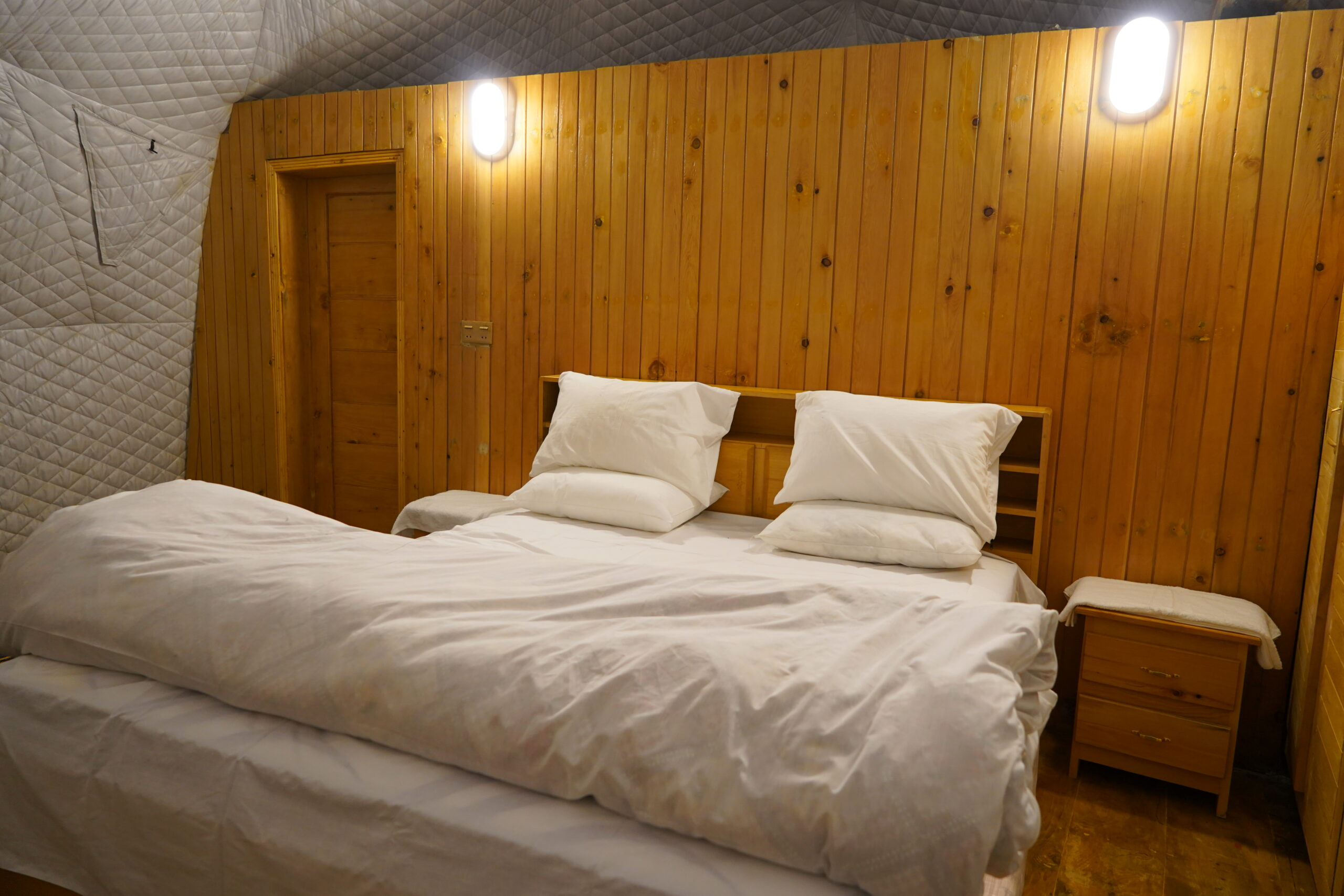 A comfortable bed inside a luxury dome accommodation in Pakistan, featuring wooden walls and warm lighting.
