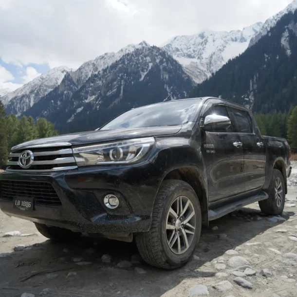 Black pickup truck in Kumrat Valley with snowy mountains.
