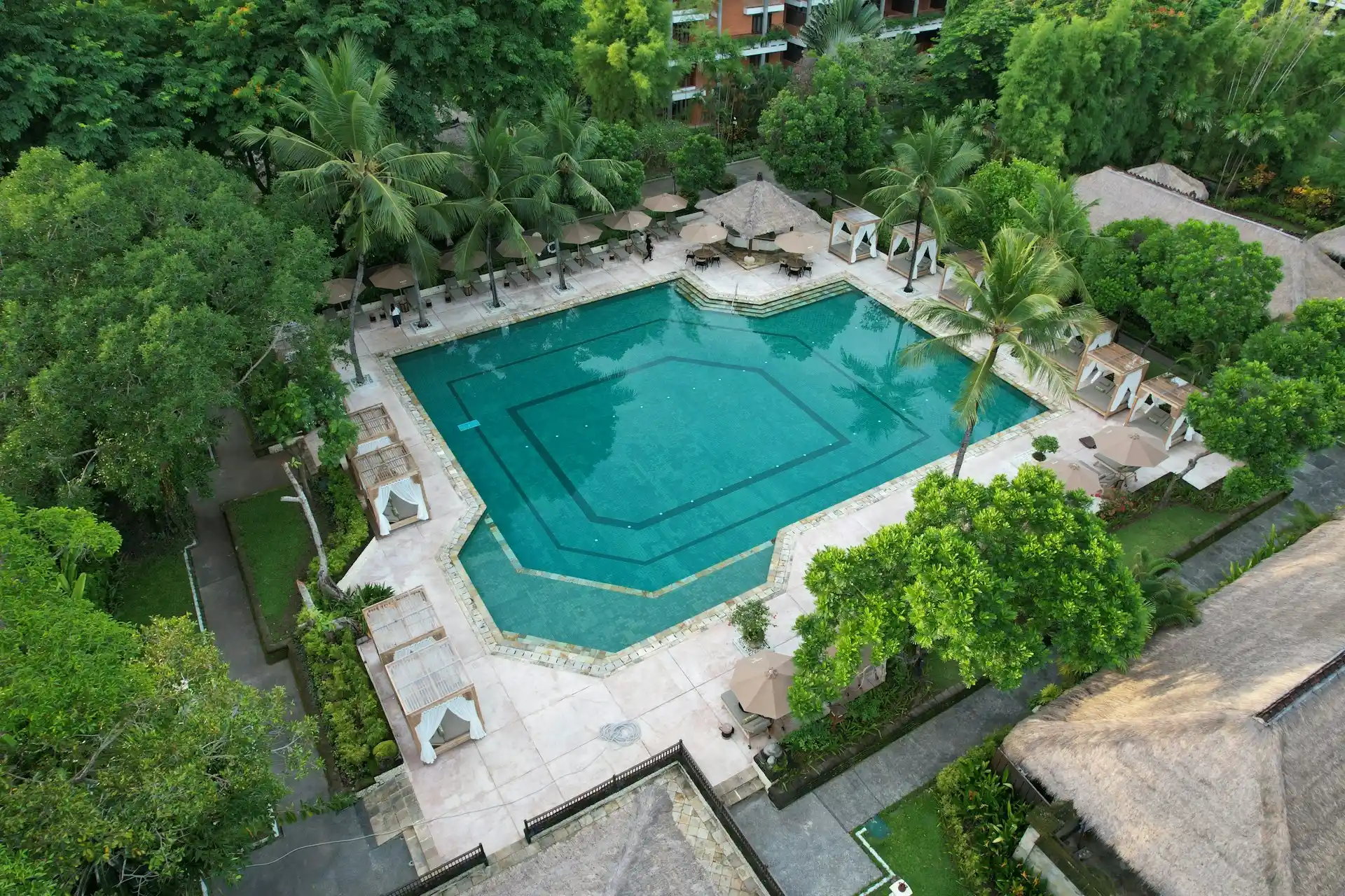 An aerial view of a large, inviting swimming pool surrounded by lush greenery and private cabanas, evoking the luxury found in resorts with private pools in Pakistan.