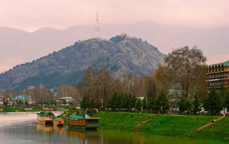 A tranquil view of houseboats on a river with a mountain in the background, a scene that represents some of the Top Resorts Near Islamabad.