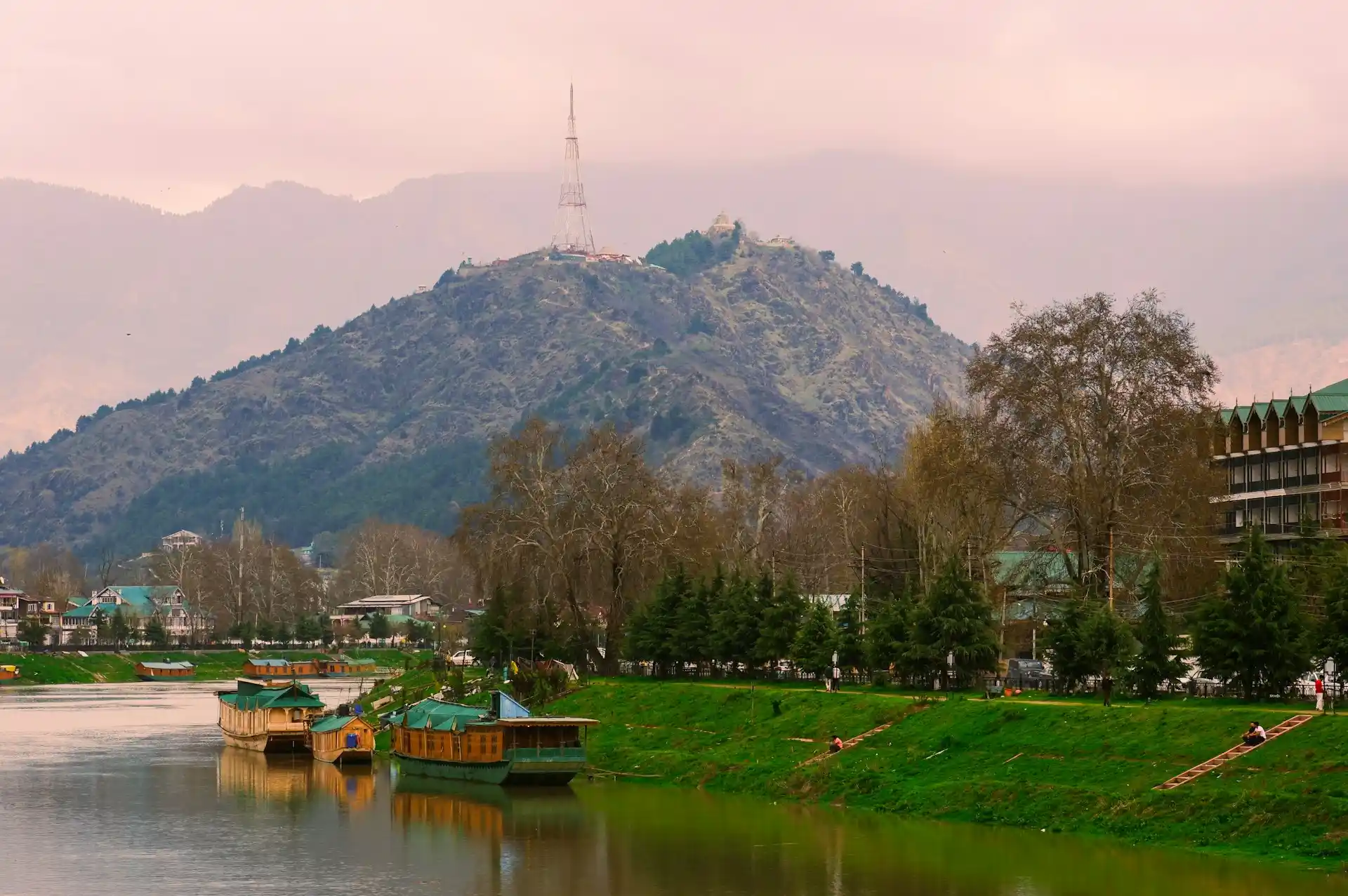 A tranquil view of houseboats on a river with a mountain in the background, a scene that represents some of the Top Resorts Near Islamabad.