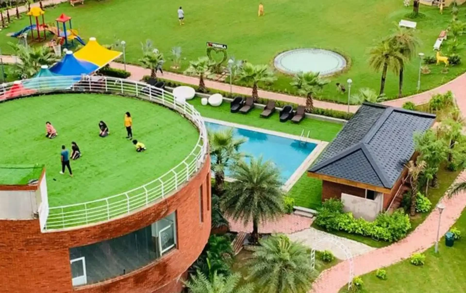 An aerial view of a resort with a swimming pool, a large grassy area with a playground, and a rooftop field, demonstrating the diverse amenities offered by Luxury Resorts with Adventure Sports Facilities in Pakistan.