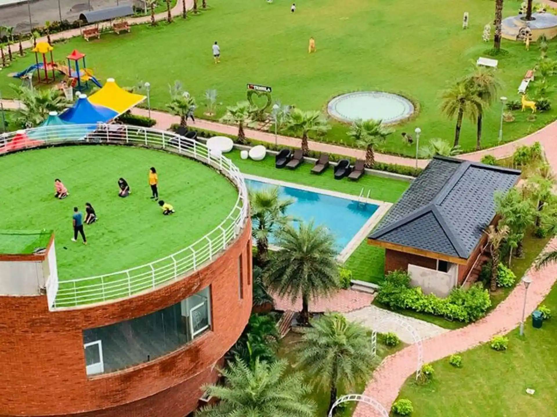 An aerial view of a resort with a swimming pool, a large grassy area with a playground, and a rooftop field, demonstrating the diverse amenities offered by Luxury Resorts with Adventure Sports Facilities in Pakistan.